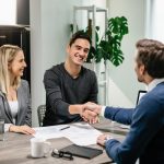Happy couple shaking hands with their real estate agent at home.